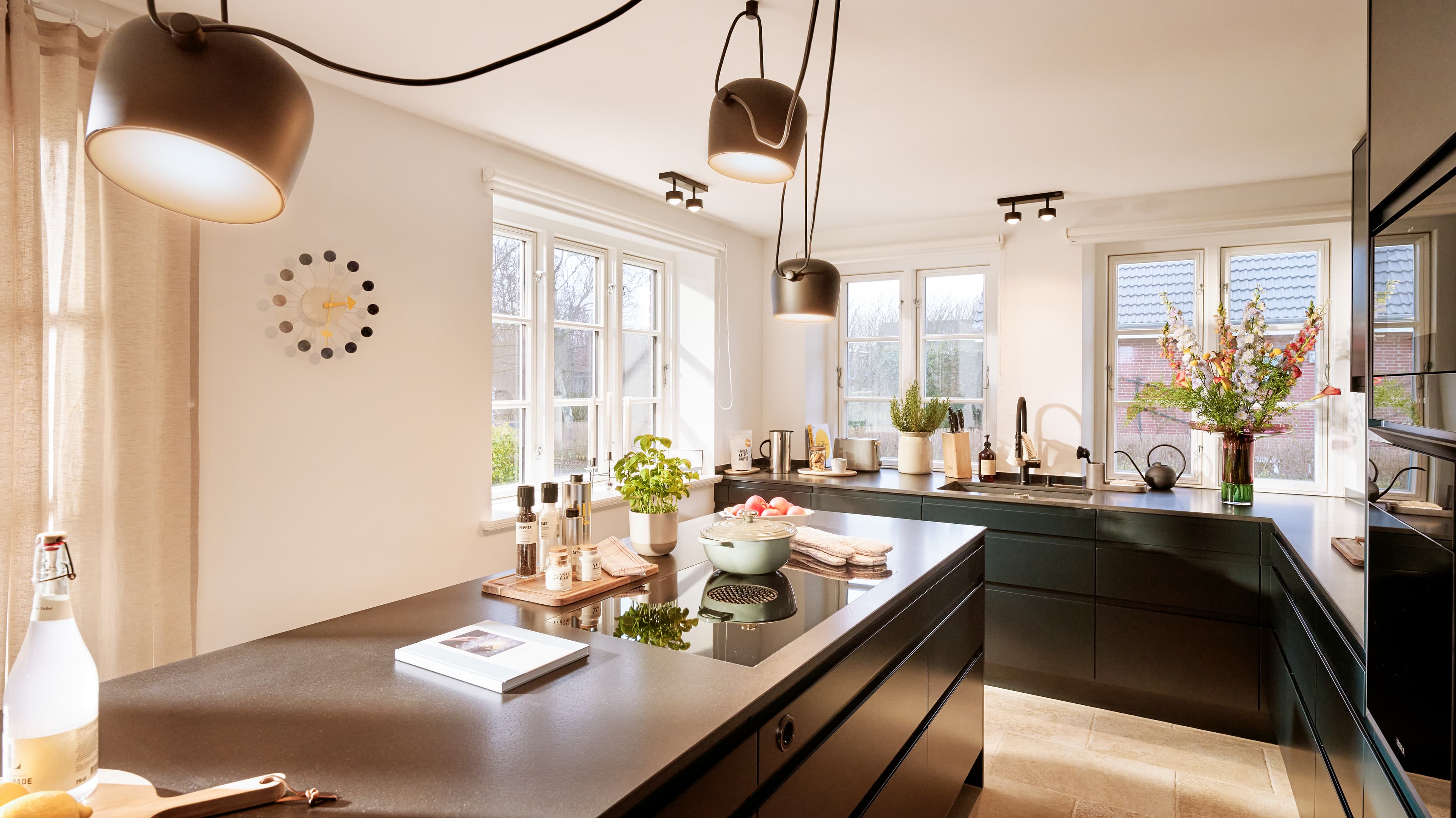 Moderne Designküche im Traumhaus auf Föhr mit Kochinsel, schwarzen Fronten und großen Fenstern.