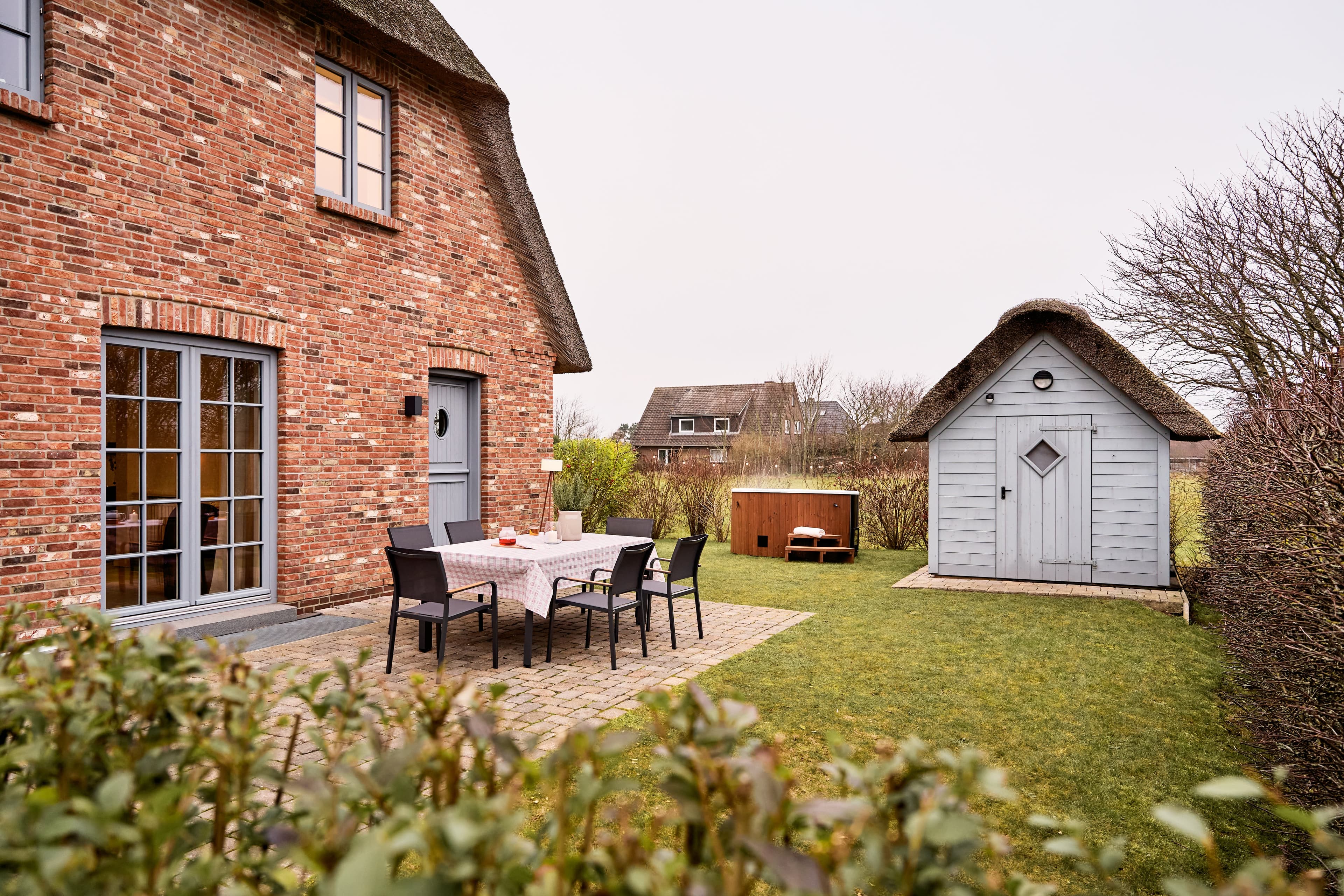 Blick in den Garten auf einer der drei Terrasse mit großem Esstisch, 6 Stühlen, Gartenhaus, Rasenfläche und Hot Tub