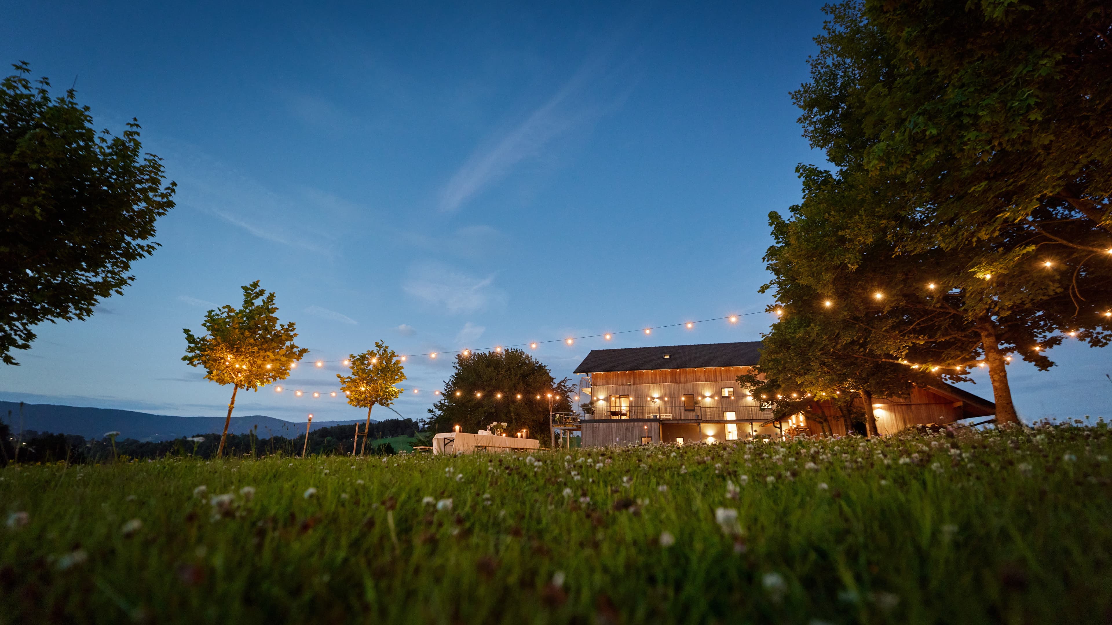 Blick auf den großen Garten mit dem Traumhaus im Hintergrund bei Abend mit Lichterketten