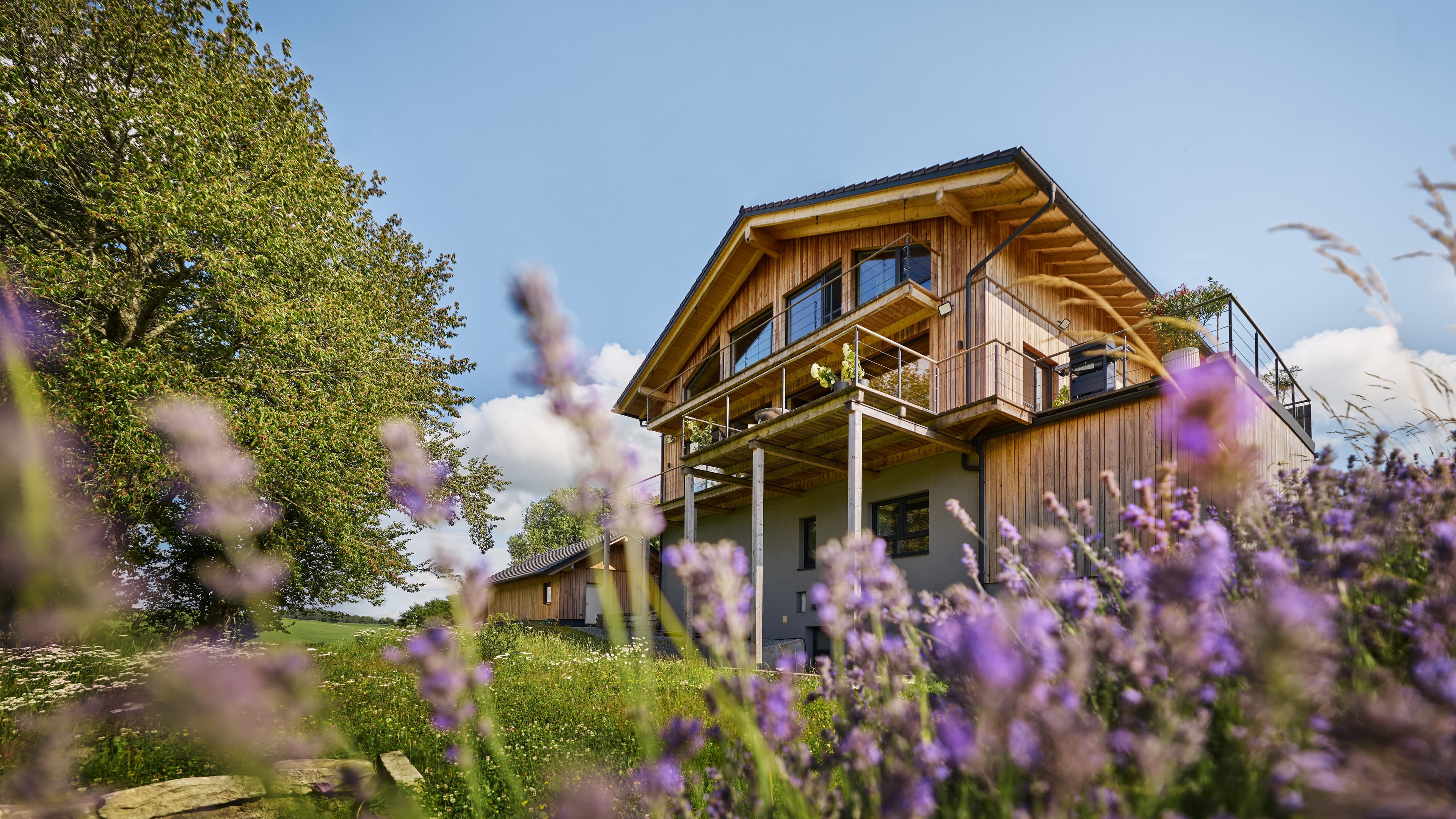 Das Traumhaus im Bayersichen Wald von Außen umgeben von lila Blumen und grünen Bäumen