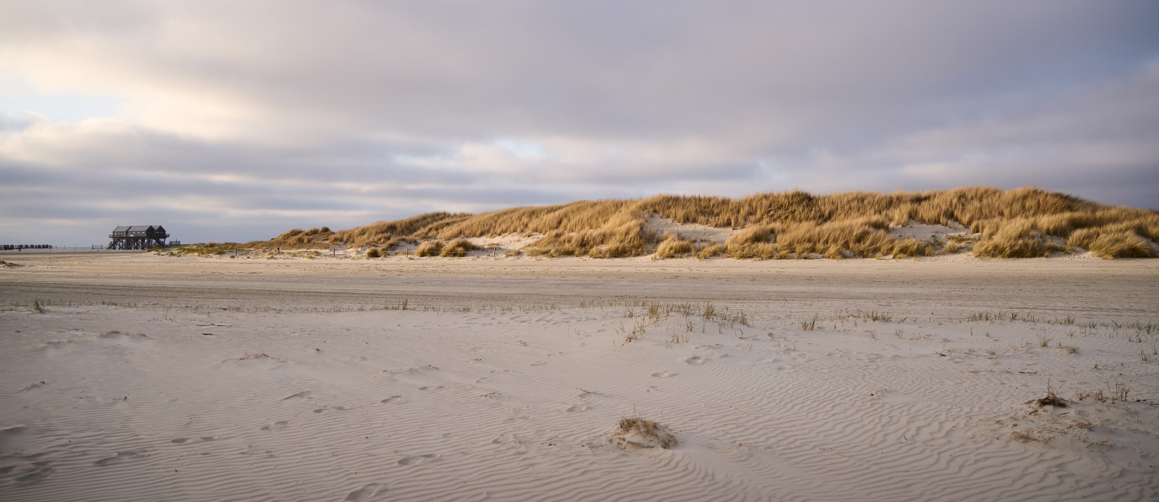 Breiter Sandstrand mit Dünenlandschaft, in der Ferne sind die berühmten Stelzenhäuser St. Peter-Ordings zu sehen