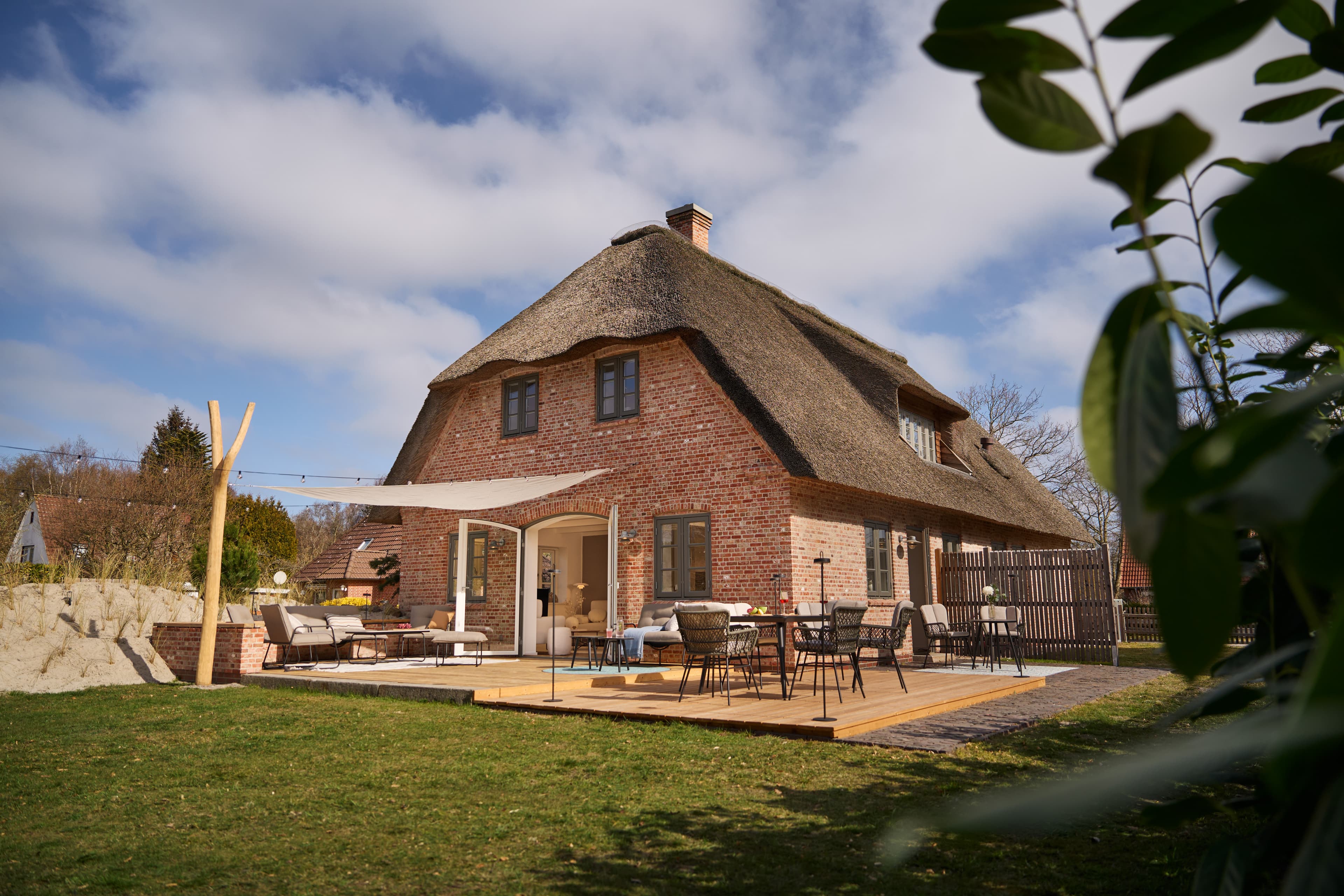 Außenansicht des Nordsee-Traumhauses mit großer Holzterrasse und Sonnensegel